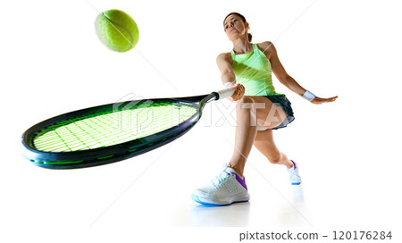 Low angle view of young woman tennis player in bright uniform stretches forward to hit ball against white studio background. Low angle view of young woman tennis player in bright uniform stretches forward to hit ball against white studio background. 120176284