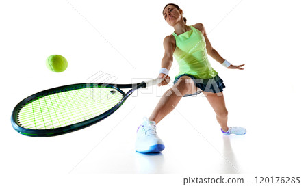 Low angle view of young woman tennis player in bright uniform stretches forward to hit ball against white studio background. Low angle view of young woman tennis player in bright uniform stretches forward to hit ball against white studio background. 120176285
