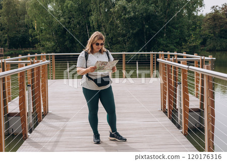 Stylish hipster woman in sunglasses holding paper map, wearing backpack and relaxing in nature. Travel and wanderlust concept. Amazing chill moment, summer time Stylish hipster woman in sunglasses holding paper map, wearing backpack and relaxing in nature. Travel and wanderlust concept. Amazing chill moment, summer time 120176316