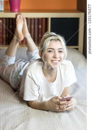 Smiling woman lying on bed using smartphone at home. 120176877