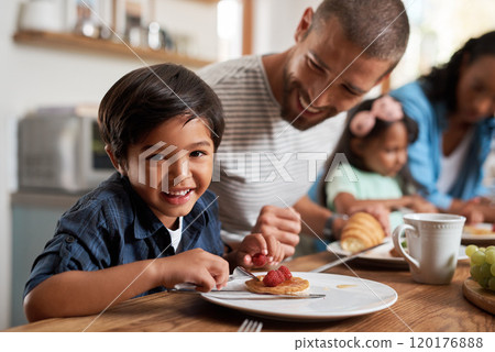 Everyone knows that I love breakfast. Portrait of an adorable little boy smiling at the camera with his family in the background. Everyone knows that I love breakfast. Portrait of an adorable little boy smiling at the camera with his family in the background. 120176888