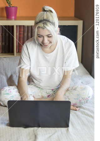 Woman sitting on bed, working on laptop, smiling. Woman sitting on bed, working on laptop, smiling. 120176919