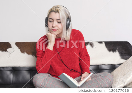 Thoughtful woman with headphones and book sitting on a couch. Thoughtful woman with headphones and book sitting on a couch. 120177016