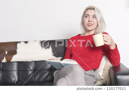 Woman in red sweater reading and holding a mug on a couch. Woman in red sweater reading and holding a mug on a couch. 120177021