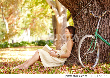 Book lovers are never alone. Shot of an attractive young woman reading a book in the park. 120177156