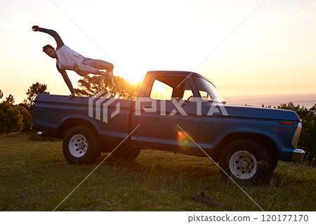 Get out there and live your life. Shot of a young man jumping out the trunk of his truck on a roadtrip. 120177170