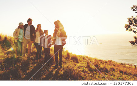 Lets make this an adventure kind of day. A multi-generational family standing on a grassy hill together at sunset with the ocean in the background. 120177302