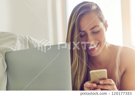 Sending her sweetheart a good morning message. Shot of a young woman using a laptop and phone in the morning at home. Sending her sweetheart a good morning message. Shot of a young woman using a laptop and phone in the morning at home. 120177383