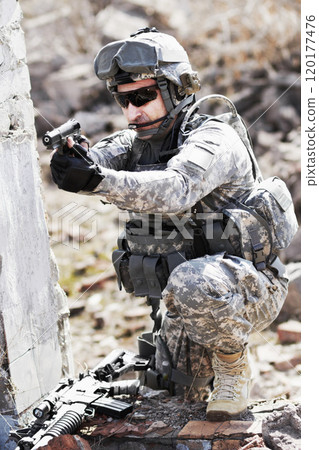 Trained in combat. A soldier crouched down next to a broken down wall and pointing his gun into the distance. Trained in combat. A soldier crouched down next to a broken down wall and pointing his gun into the distance. 120177476