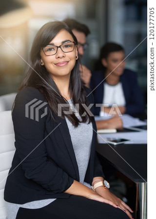 Succeeding is my top priority. Portrait of a smiling young businesswoman sitting in an office with colleagues in the background. 120177705