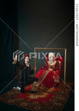 Young man, court medieval servant taking selfie with smartphone with elderly countess places in golden picture frame. 120178511