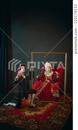 Young man, court medieval servant taking selfie with smartphone with elderly countess places in golden picture frame. 120178512