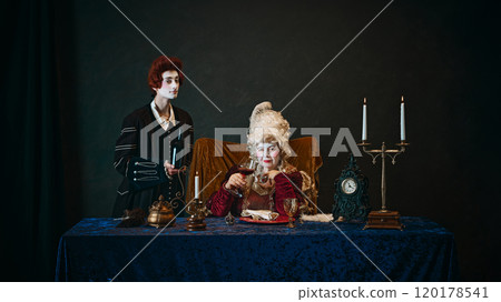 Portrait of elderly woman with colorful makeup and wig, medieval empress with glass of red wine sitting at table with her young servant standing near Portrait of elderly woman with colorful makeup and wig, medieval empress with glass of red wine sitting at table with her young servant standing near 120178541