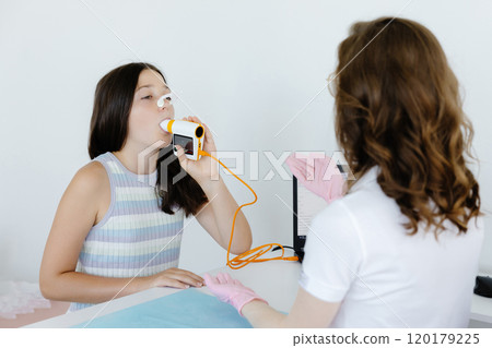 Girl testing breathing function by spirometry in doctors office. Diagnosis of respiratory function in pulmonary disease 120179225