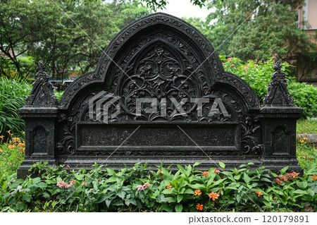 gothic style granite headstone features arched top adorned ornate carvings and motifs. Surrounded lush greenery it maintains solemn presence bright white backdrop. 120179891