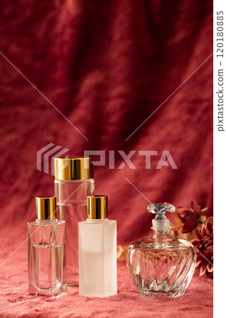 Glass cosmetic containers and vintage perfume bottles lined up against a red fabric background 120180885