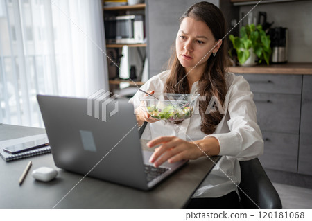 Tired woman eats food ordered at delivery service while sitting in her home office in front of laptop during lunch break. Tired woman eats food ordered at delivery service while sitting in her home office in front of laptop during lunch break. 120181068