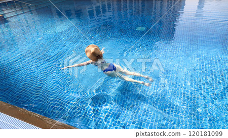 Woman in blue bikini and straw hat swimming in pool 120181099