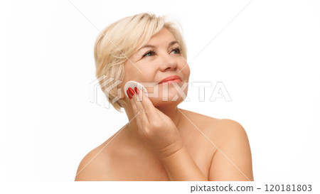 Mature beautiful blonde woman wipes face with cotton pad to remove make up against white studio background. Mature beautiful blonde woman wipes face with cotton pad to remove make up against white studio background. 120181803