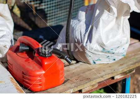 A red gas can sits on a wooden table next to a white bag A red gas can sits on a wooden table next to a white bag 120182225