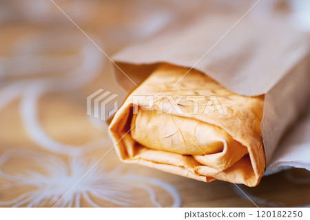 A delicious burrito is wrapped in brown paper and placed on a table 120182250