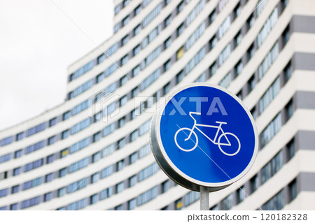 A blue sign featuring a bicycle graphic stands in front of a building 120182328