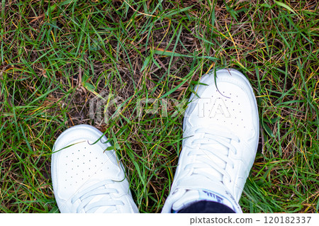 A persons feet are positioned in the grass while wearing white Nike shoes A persons feet are positioned in the grass while wearing white Nike shoes 120182337