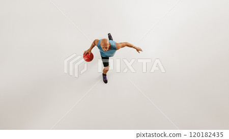 Aerial view of male basketball athlete dribbles basketball preparing for jump against grey studio background. 120182435