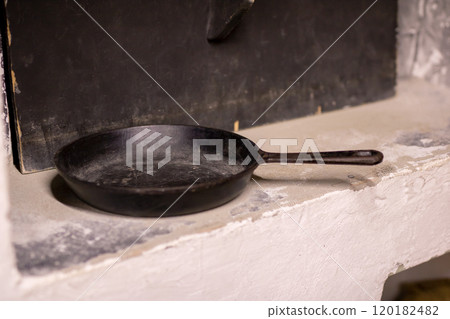 A cast iron skillet is resting on a ledge right in front of a fireplace A cast iron skillet is resting on a ledge right in front of a fireplace 120182482