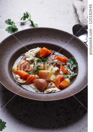 Chicken soup with potatoes and carrots in brown plate, dark background. Comfort food concept. 120182648