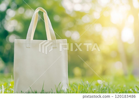 A white tote bag on grass, surrounded by trees and sunlight, ideal for logo mockups. A white tote bag on grass, surrounded by trees and sunlight, ideal for logo mockups. 120183486