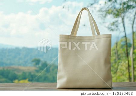 A simple canvas tote bag sits peacefully in a lush forest, complementing the tranquil blue sky and nature's calm. 120183498