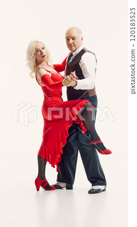 Romantic anniversary. Elderly beautiful woman and handsome man in red dress and black suit, dancing tango isolated on white background 120183525