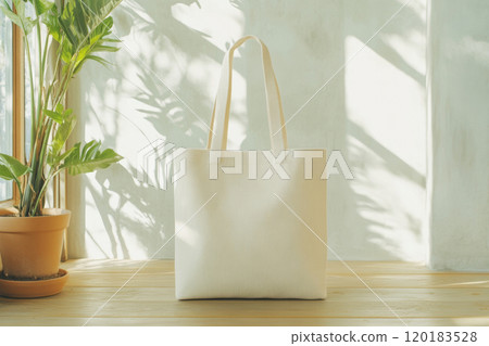A stylish canvas tote bag is highlighted in a bright, minimalist space with natural light and greenery. 120183528