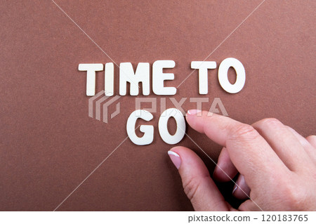 Time To Go. White letters of the alphabet and a woman's hand on a brown background 120183765