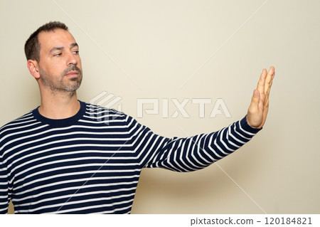 Close-up side profile photo of a man in a serious and defiant attitude, extending one arm and making a stop sign. Isolated on beige studio background. 120184821