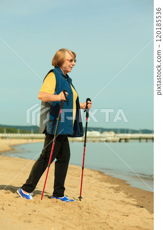active woman senior nordic walking on a beach 120185536