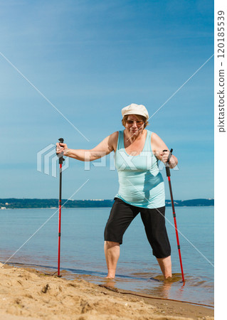 Senior woman practicing nordic walking on beach Senior woman practicing nordic walking on beach 120185539