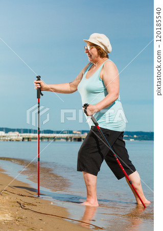 Senior woman practicing nordic walking on beach 120185540