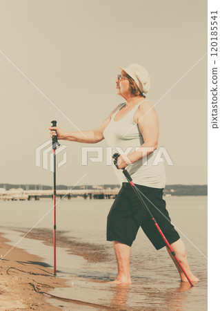 Senior woman practicing nordic walking on beach 120185541