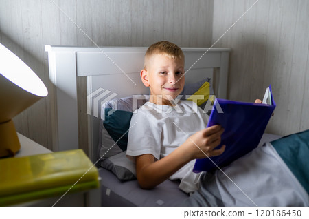 fair-haired teenage boy reading a book before bed 120186450