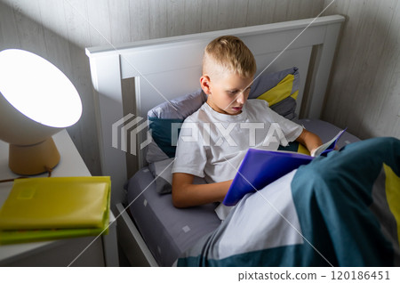 fair-haired teenage boy reading a book before bed 120186451