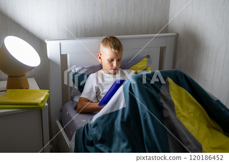 fair-haired teenage boy reading a book before bed 120186452