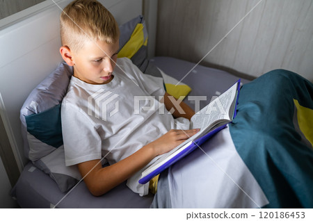 fair-haired teenage boy reading a book before bed 120186453