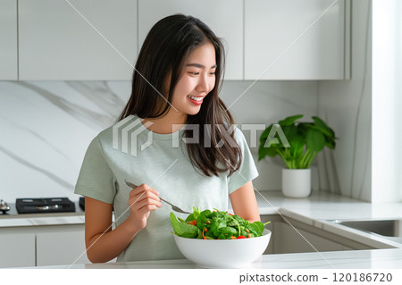 Asian woman eating salad in a light kitchen, healthy eating concept Asian woman eating salad in a light kitchen, healthy eating concept 120186720