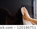 Man wiping dust on plasma panel with white cloth. A hand is seen wiping a glossy black surface with a white cloth, highlighting the effort to maintain cleanliness in a well-lit indoor space. 120186751