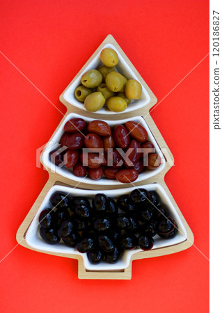 Green, black and red olives in a vase in the shape of a Christmas tree on a red background 120186827