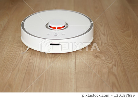 Top view of white wireless autonomous robotic vacuum cleaner on wooden floor. Smart cleaning technology. Self-propelled cleaning robot. Floor cleaning system. Household remote control appliances. Top view of white wireless autonomous robotic vacuum cleaner on wooden floor. Smart cleaning technology. Self-propelled cleaning robot. Floor cleaning system. Household remote control appliances. 120187689