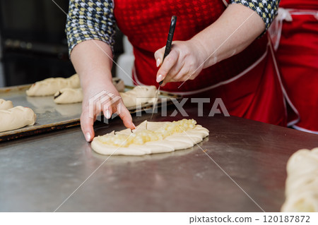 Hands skillfully scoring dough filled with apple topping, preparing for baking perfection Hands skillfully scoring dough filled with apple topping, preparing for baking perfection 120187872