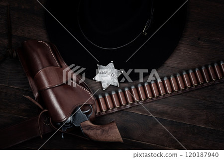 Old west sheriff star badge with gun, holster and gun belt with old west hat on table. Top view. 120187940